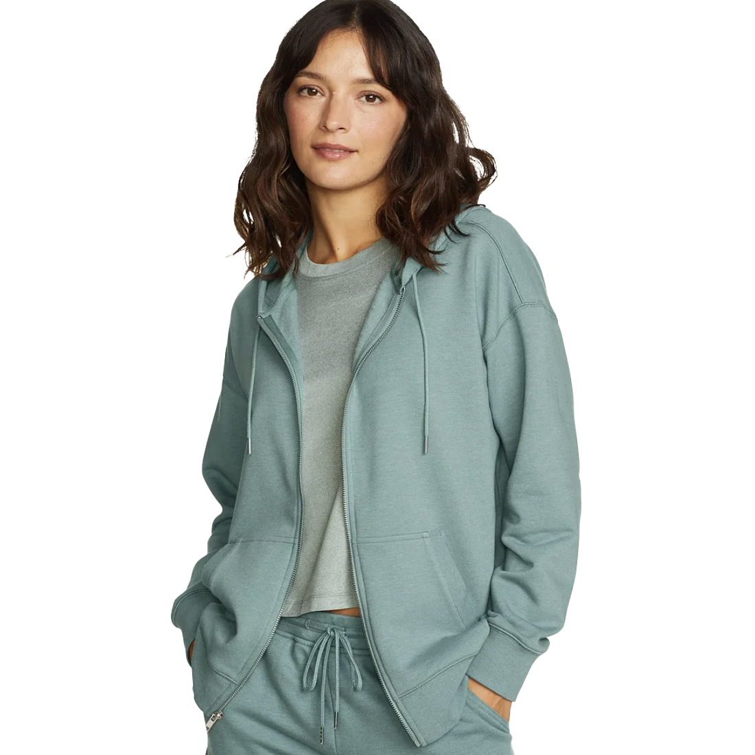 A woman wears a soft, teal-colored hooded jacket with front pockets and a zip closure, paired with matching drawstring pants.