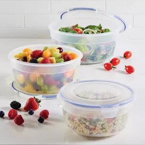 Three round, clear plastic food storage containers with blue sealing lids are shown, containing assorted fruits, salad, and a pasta dish. Scattered around are cherry tomatoes and various berries.