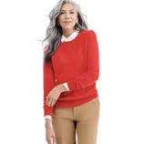 A person wearing a red sweater paired with a white collared shirt and beige pants, accessorized with earrings and a ring.