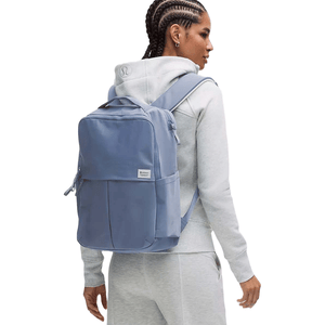 A person wearing a gray hoodie is carrying a blue Lululemon backpack, showcasing its size and shoulder strap design.