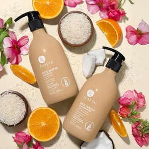 Luseta Rice Water Shampoo and Conditioner are shown with rice, coconut, orange slices, and pink flowers for a natural aesthetic.