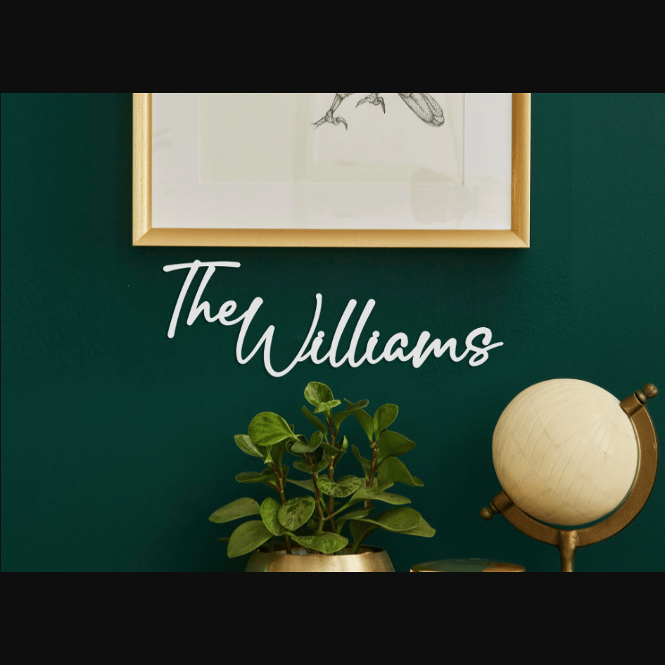 A wall decor sign reads \“The Williams\“ in white script, mounted on a dark green wall. Below it, there's a plant in a gold pot and a small globe, along with a framed insect illustration above.