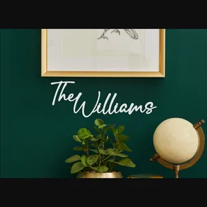 A wall decor sign reads \“The Williams\“ in white script, mounted on a dark green wall. Below it, there's a plant in a gold pot and a small globe, along with a framed insect illustration above.