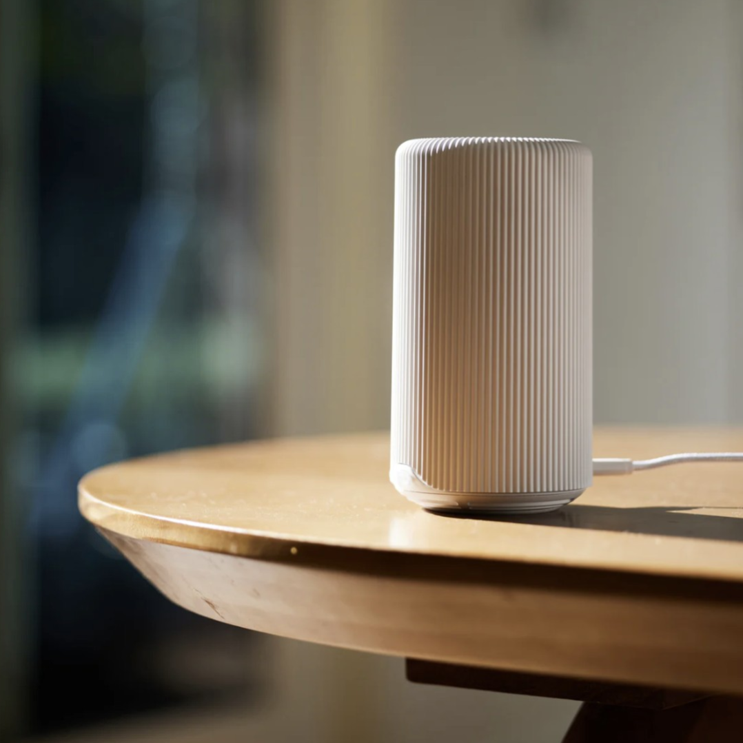 A cylindrical, white, ribbed electronic device is plugged in and placed on a wooden table.