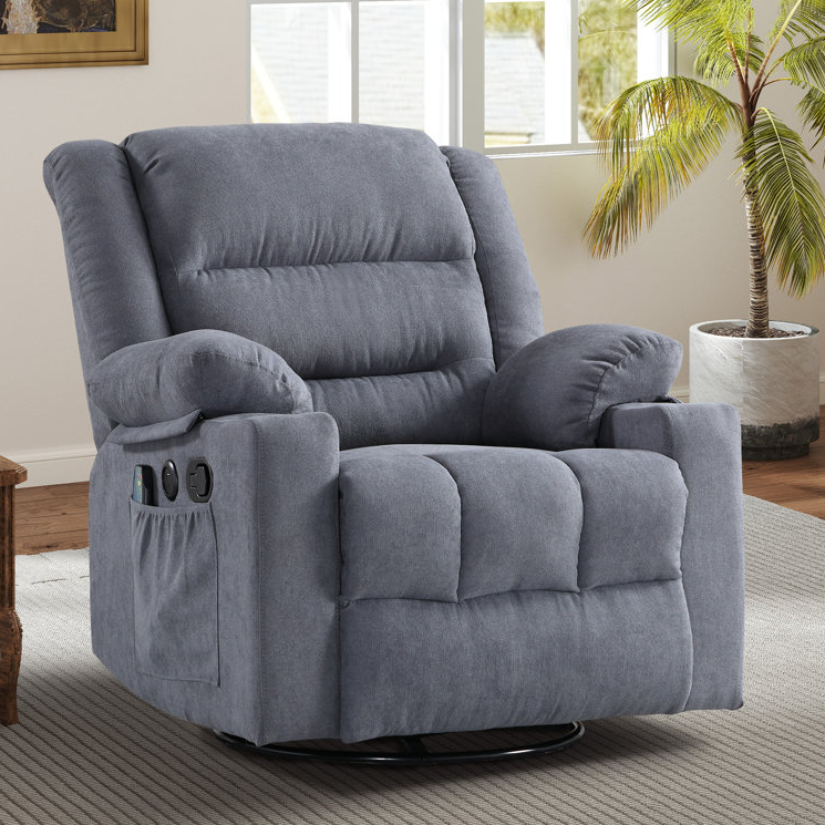 Gray plush reclining chair with padded armrests, offering massage and heat features. Includes side-mounted USB ports and a storage pocket, placed in a cozy, sunlit room with a palm plant nearby.