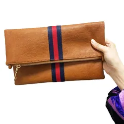 A brown fold-over clutch with a blue and red stripe detail, featuring a zipper closure, is held in a hand.
