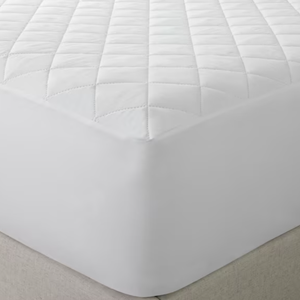 White quilted mattress pad on a bed.