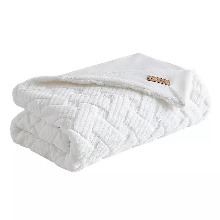 A folded white plush blanket with a subtle geometric pattern and a small leather tag.