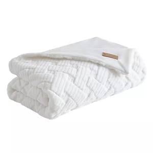 A folded white plush blanket with a subtle geometric pattern and a small leather tag.