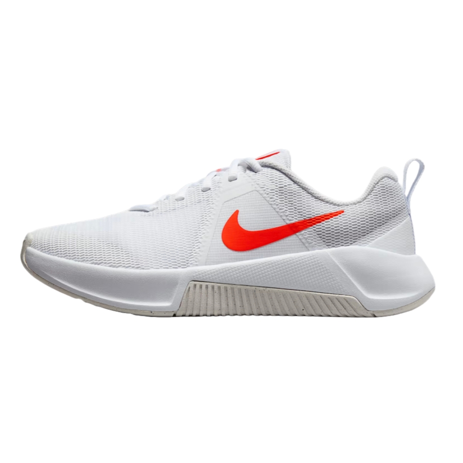 White Nike MC Trainer shoes with a mesh upper, featuring an orange Swoosh logo on the side. They have a sturdy midsole and a heel tab for easy wear.