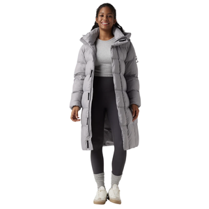 A person wears a long, light gray puffer coat over a light gray shirt with dark gray leggings, gray socks, and white sneakers.