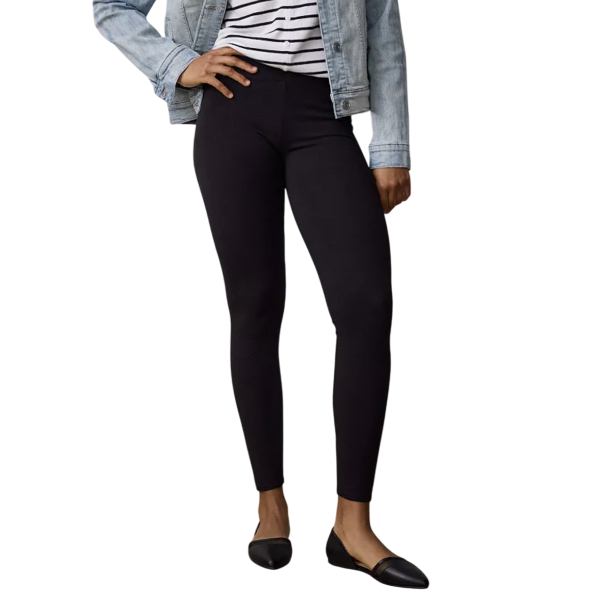 A person is wearing black leggings, a striped shirt, a light denim jacket, and black flats, standing on a wooden floor.