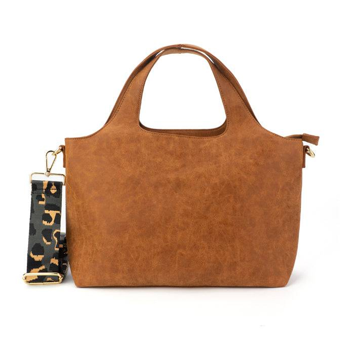 A brown leather tote bag with integrated handles and a detachable strap featuring a dark, patterned design.