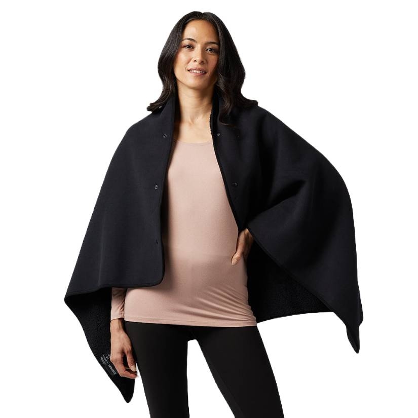 A woman wearing a black cape-style jacket over a beige shirt and black leggings stands against a plain background.