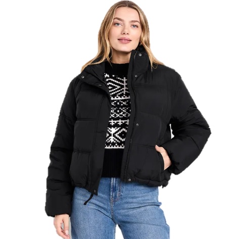 A woman is wearing a black puffer jacket over a black and white patterned sweater and blue jeans.