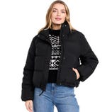 A woman is wearing a black puffer jacket over a black and white patterned sweater and blue jeans.