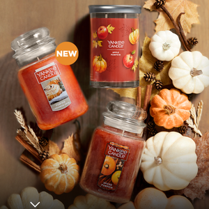 Three Yankee Candles with autumn-themed scents surrounded by seasonally appropriate decorations like pumpkins and leaves.