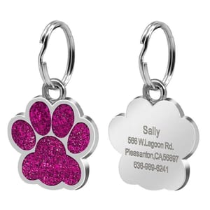 A silver paw-shaped pet tag with a pink glitter design on the front and personalized engraving on the back, including a name, address, and phone number.