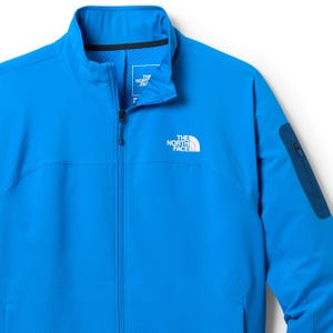 A bright blue zip-up jacket from The North Face, featuring a stand-up collar and a zippered pocket on the sleeve.