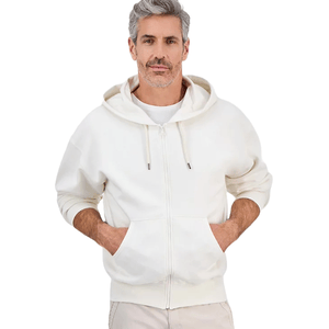 A man wears a white zip-up hoodie with a front pocket and drawstrings, paired with light-colored pants.
