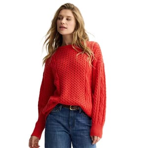 A woman is wearing a red, knit sweater with a cable pattern paired with blue jeans.