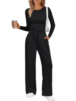 A person wearing a black, long-sleeve, drawstring loungewear set with wide-leg pants and white sneakers, holding a coffee cup and carrying a white shoulder bag.