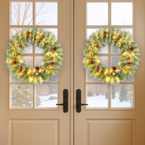 Two festive wreaths with lights hang on glass-paneled double doors, flanked by decorated Christmas trees in baskets. Snow is visible through the doors, enhancing the holiday ambiance.
