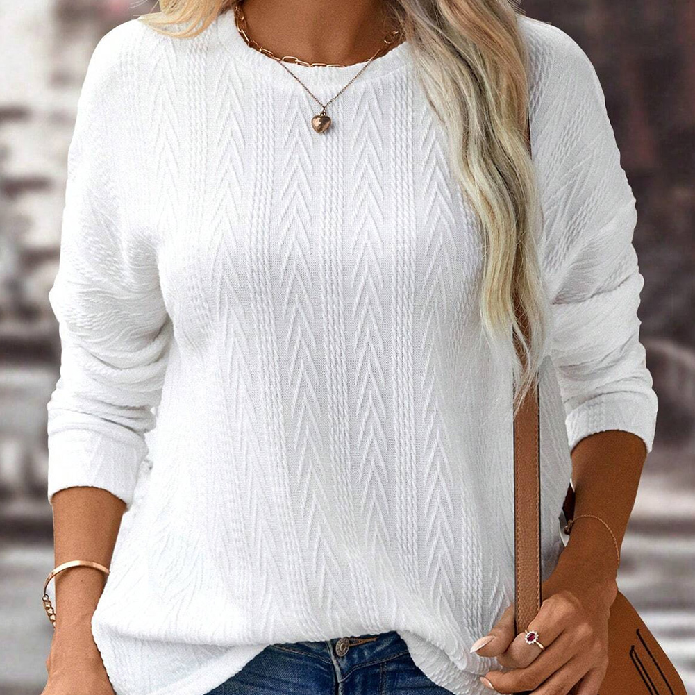 Woman wearing a white textured sweater, accessorized with a necklace and a leather strap watch, holding a tan purse.