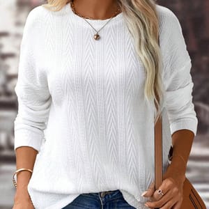 Woman wearing a white textured sweater, accessorized with a necklace and a leather strap watch, holding a tan purse.