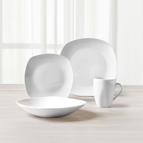 A set of white dinnerware, including two plates of different sizes, a bowl, and a mug, on a wooden surface.