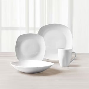 A set of white dinnerware, including two plates of different sizes, a bowl, and a mug, on a wooden surface.