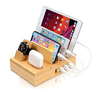 Bamboo charging station holding an iPad, two smartphones, a smartwatch, and wireless earbuds, with multiple charging cables connected.