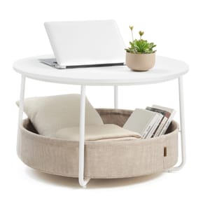 A round coffee table with a white top holds a laptop and a small potted plant. Below, a fabric-covered pet bed and storage space with books are integrated into the design.