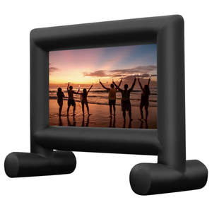 An inflatable movie screen with a black frame displays an image of people holding sparklers on a beach at sunset.