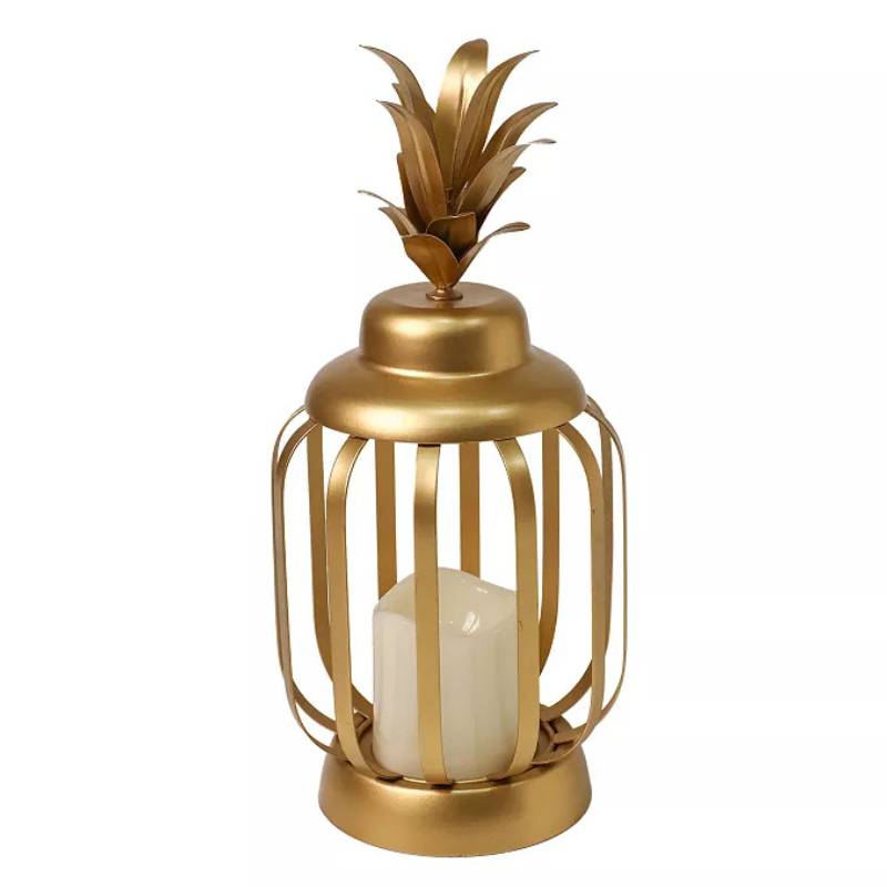 A gold metal lantern with a decorative lid resembling pineapple leaves, containing a white candle inside.