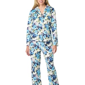 A woman wearing floral-patterned pajamas with a mix of blue, white, and green colors. The set includes a long-sleeve top and matching pants.