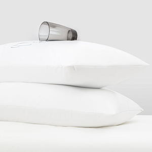 Two white jersey knit pillow protectors with a spilled glass of water on top, demonstrating water resistance.