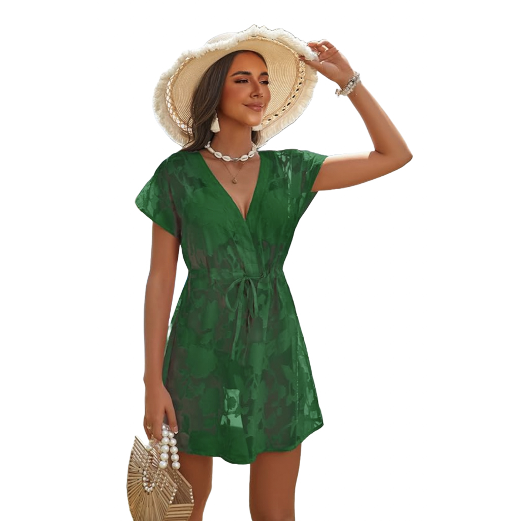 A woman wears a green, floral lace swim cover-up with short sleeves and a tie waist, complemented by a wide-brimmed straw hat, beaded jewelry, and a straw handbag with pearl accents.
