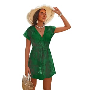 A woman wears a green, floral lace swim cover-up with short sleeves and a tie waist, complemented by a wide-brimmed straw hat, beaded jewelry, and a straw handbag with pearl accents.