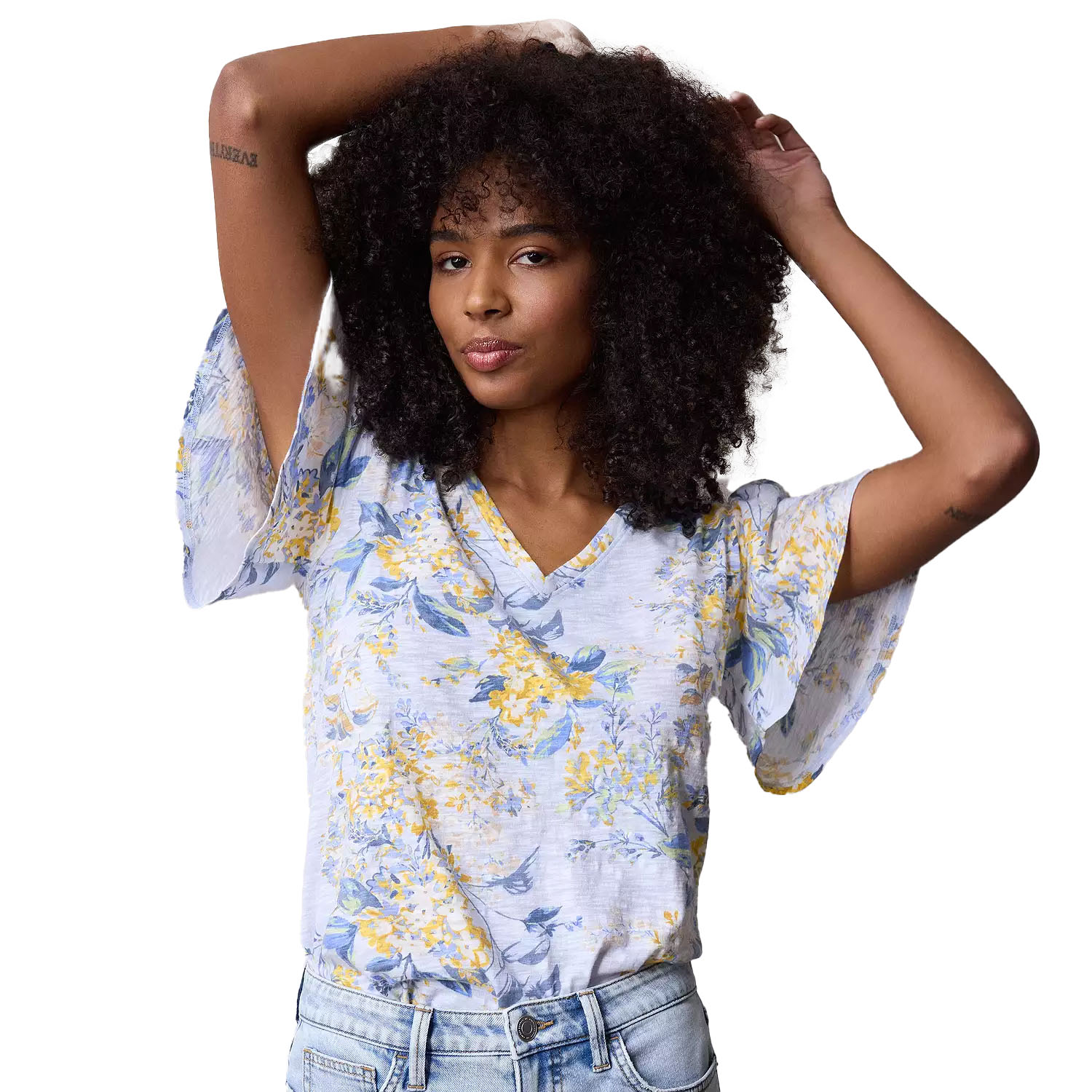 A floral V-neck top with flutter sleeves, featuring a soft, light blue and yellow floral pattern. Paired with light blue jeans.