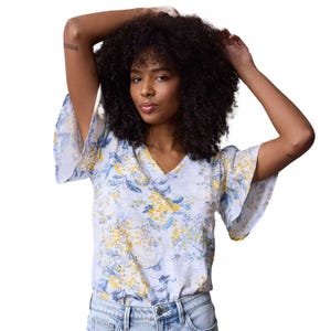 A floral V-neck top with flutter sleeves, featuring a soft, light blue and yellow floral pattern. Paired with light blue jeans.