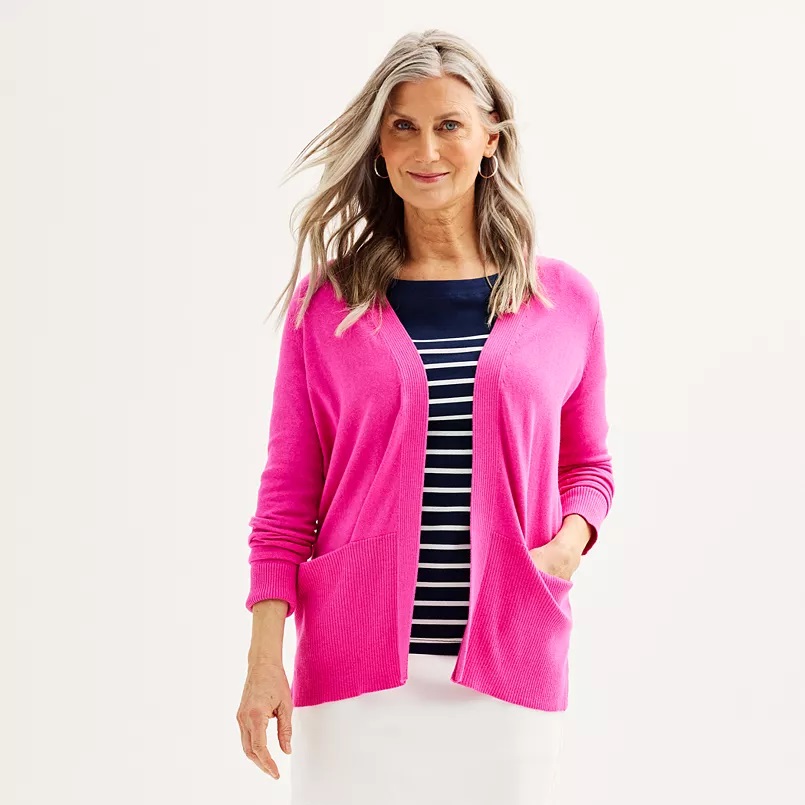 A woman is wearing a bright pink cardigan over a navy and white striped top, paired with hoop earrings.