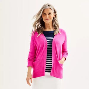 A woman is wearing a bright pink cardigan over a navy and white striped top, paired with hoop earrings.
