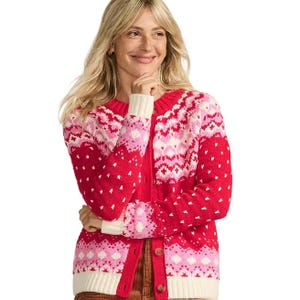 A woman is wearing a red and pink patterned cardigan with a button-up front and ribbed cuffs, featuring a Nordic-inspired design.