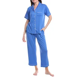 A woman is wearing a blue short-sleeve pajama set with white piping, featuring a button-up top with a chest pocket and relaxed-fit pants.
