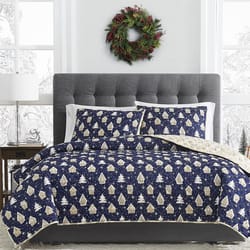 3pc Reversible Gingerbread Quilt Set features a navy quilt and pillow shams with beige gingerbread house and tree designs, reversible to a light beige snowflake pattern, complemented by a gray tufted headboard and festive wreath above.