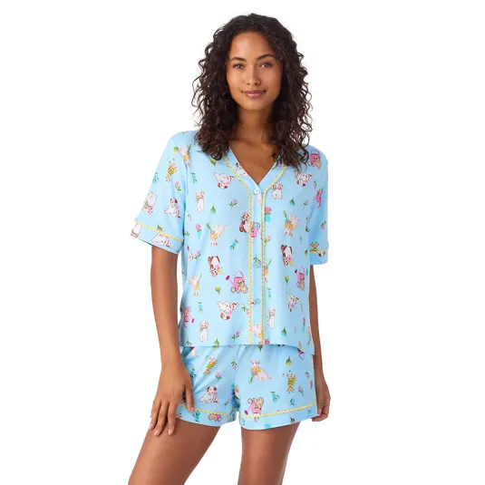 A woman is wearing a light blue pajama set featuring short sleeves and shorts, covered in playful animal prints and small decorative elements.