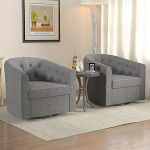 Two gray swivel accent chairs with a tufted design and curved armrests are set on a beige patterned rug. They are positioned around a small round side table with decorative items, under a framed wall picture and next to a floor lamp.