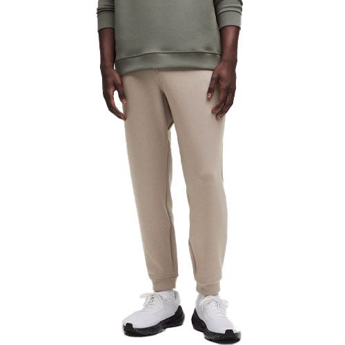 A person wearing beige jogger pants paired with a green top and white sneakers with black soles.