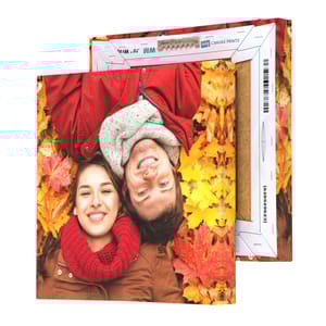 A canvas print showing a couple lying in autumn leaves, with the canvas wrapping extending around the sides of the wooden frame.